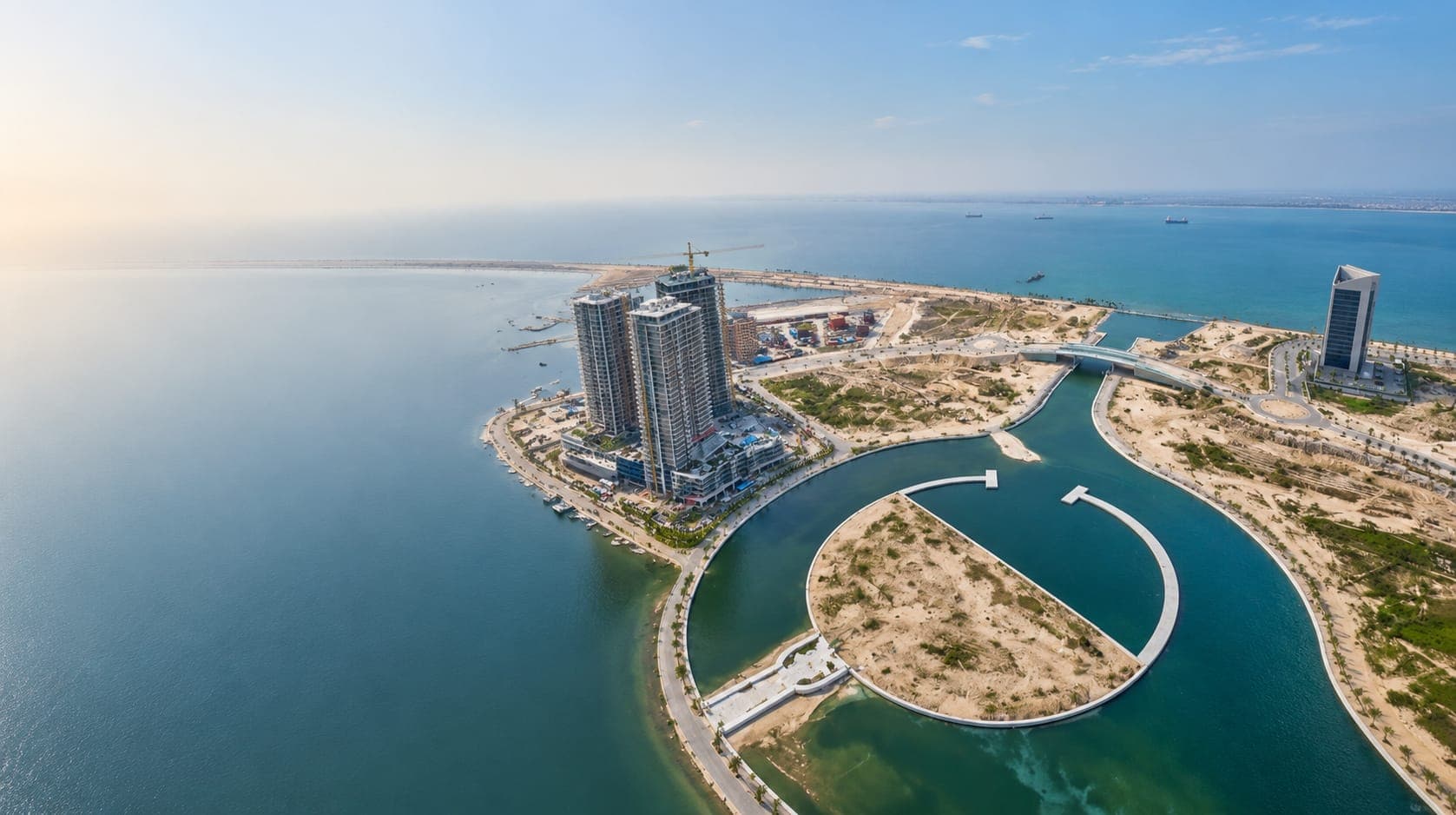 Aerial view of a waterfront development, with high-rise towers and reclaimed land reaching into the sea